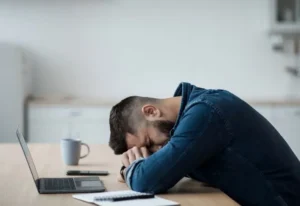 A-person-is-sleeping-on-a-table-in-front-of-a-laptop