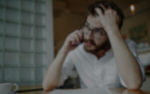 A person with glasses sits at a table and talks on the phone